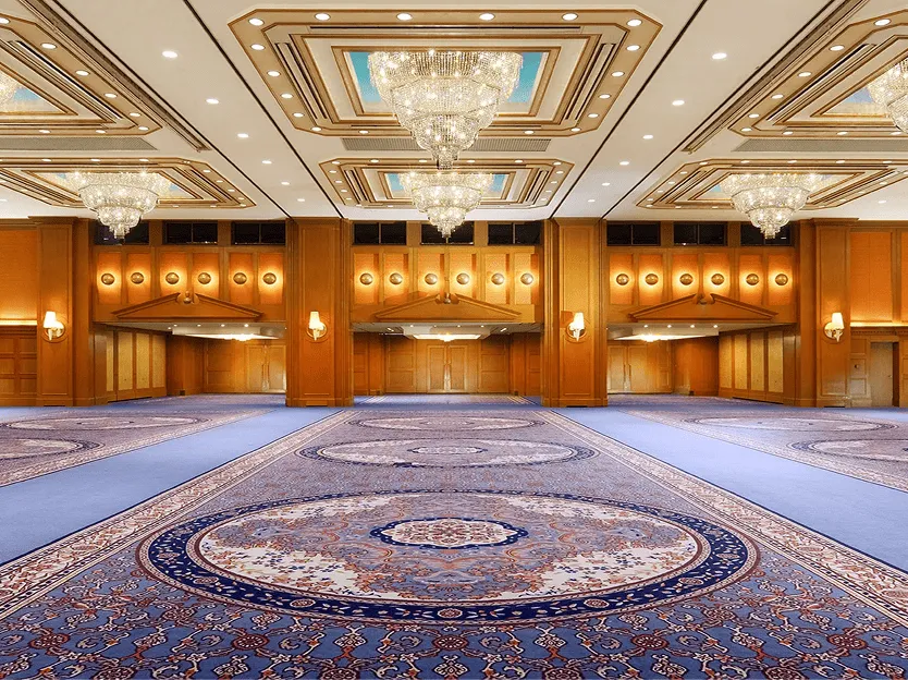 名古屋観光ホテルの那古の間の写真。複数のシャンデリアが輝く高い天井と、青地に大きな円形模様の絨毯が敷き詰められた広大なイベント空間。